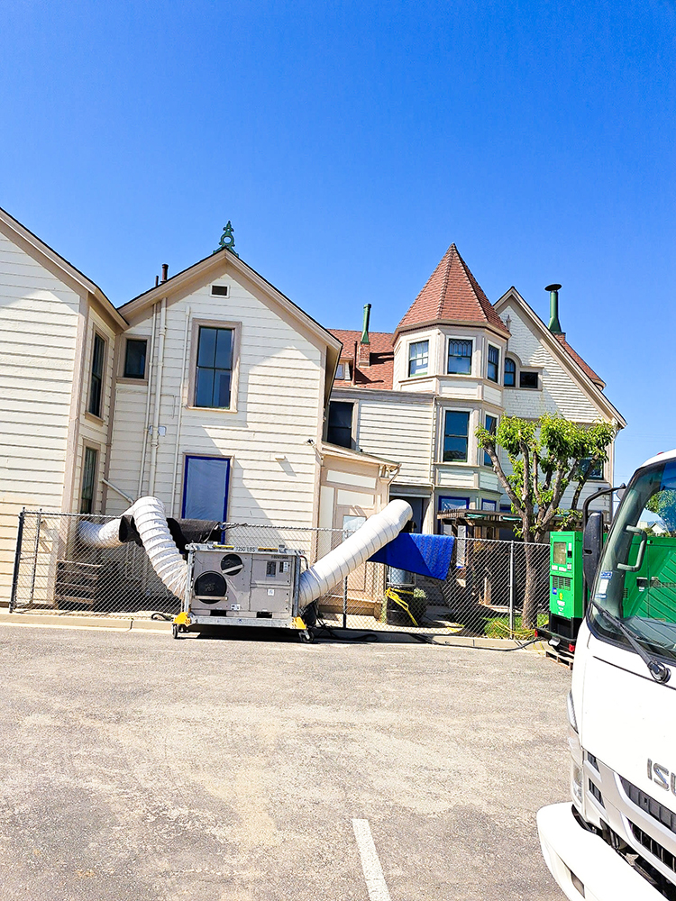 Air scrubber and long hoses attached to a large, light-colored building.