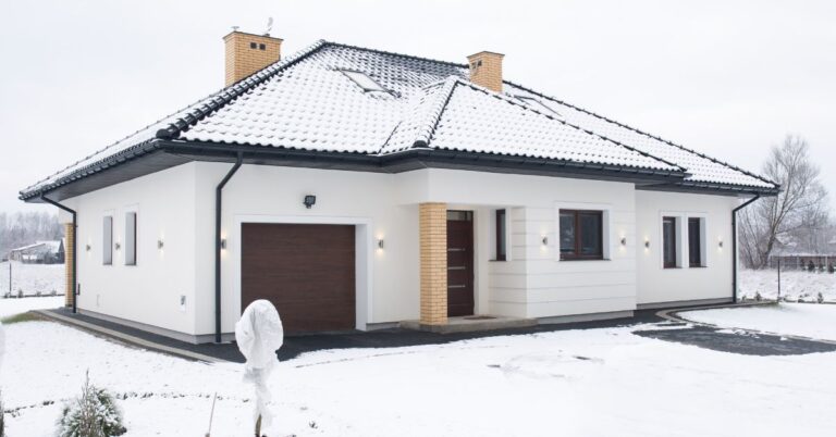 A snow-covered white house with a brown garage door and brick accents.