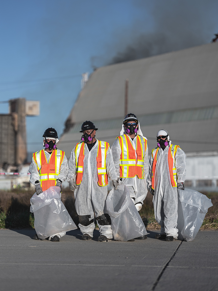 Four people in hazmat suits and respirators carrying large plastic bags.