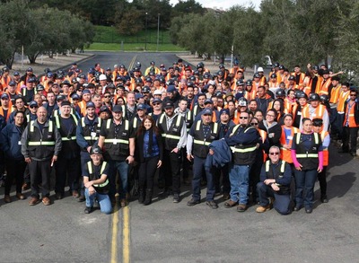 Large group of people wearing safety vests and hard hats posing for a photo.