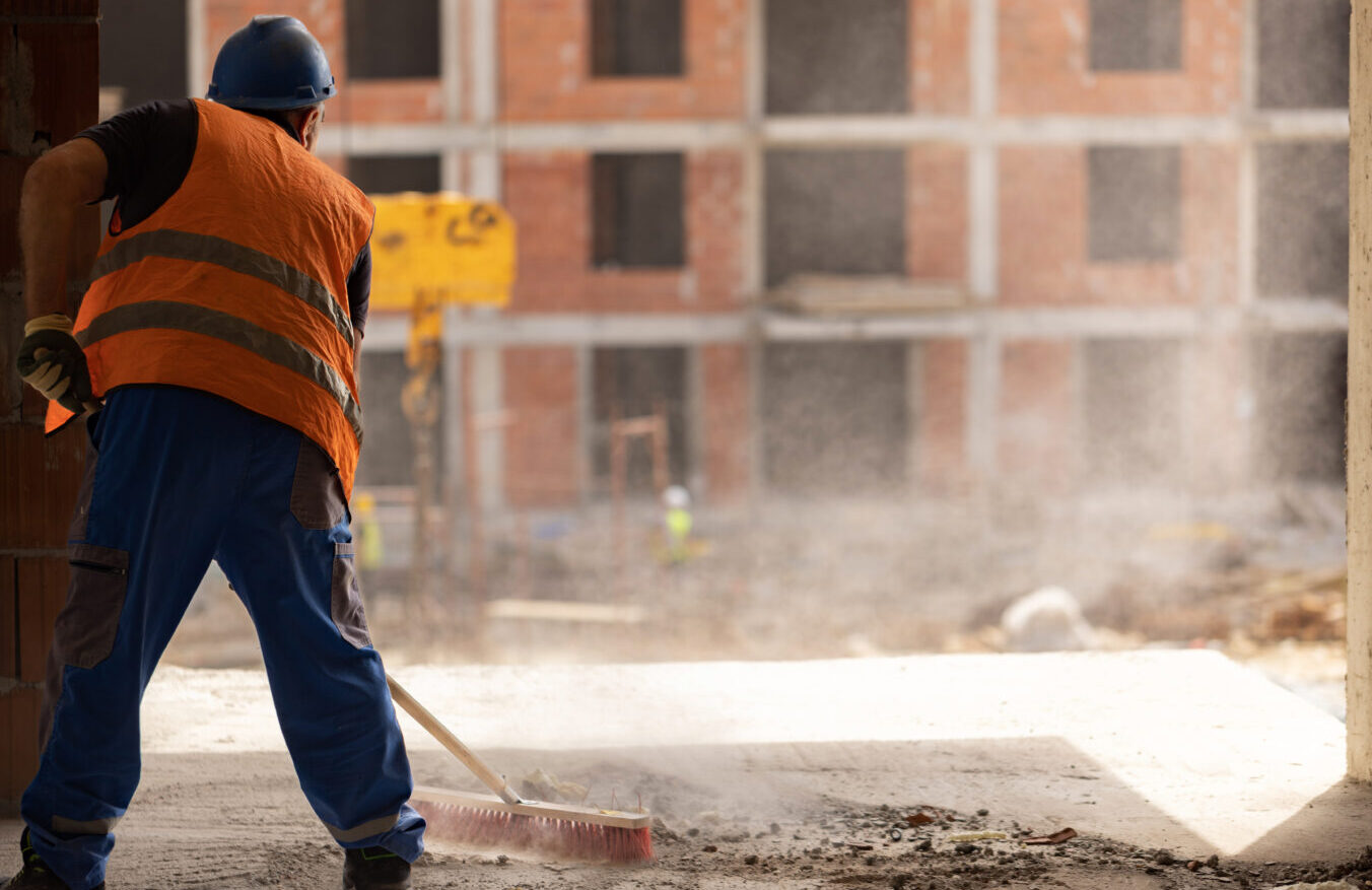 Unrecognizable mid-adult construction worker, using broom, to clean the dust on the construction site