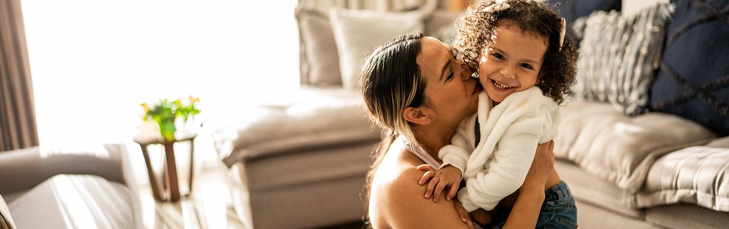 A mother lovingly kisses her young daughter.