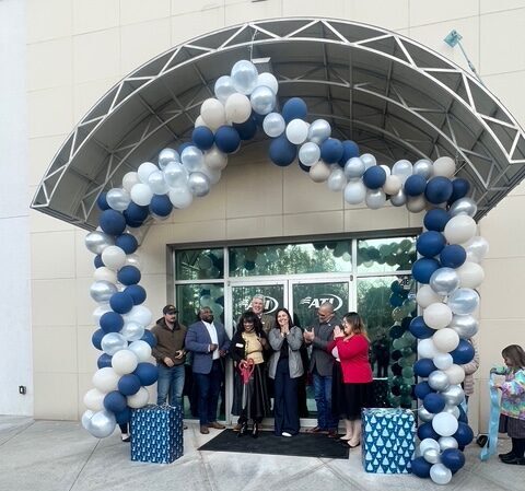Grand opening celebration with people gathered under a balloon arch.