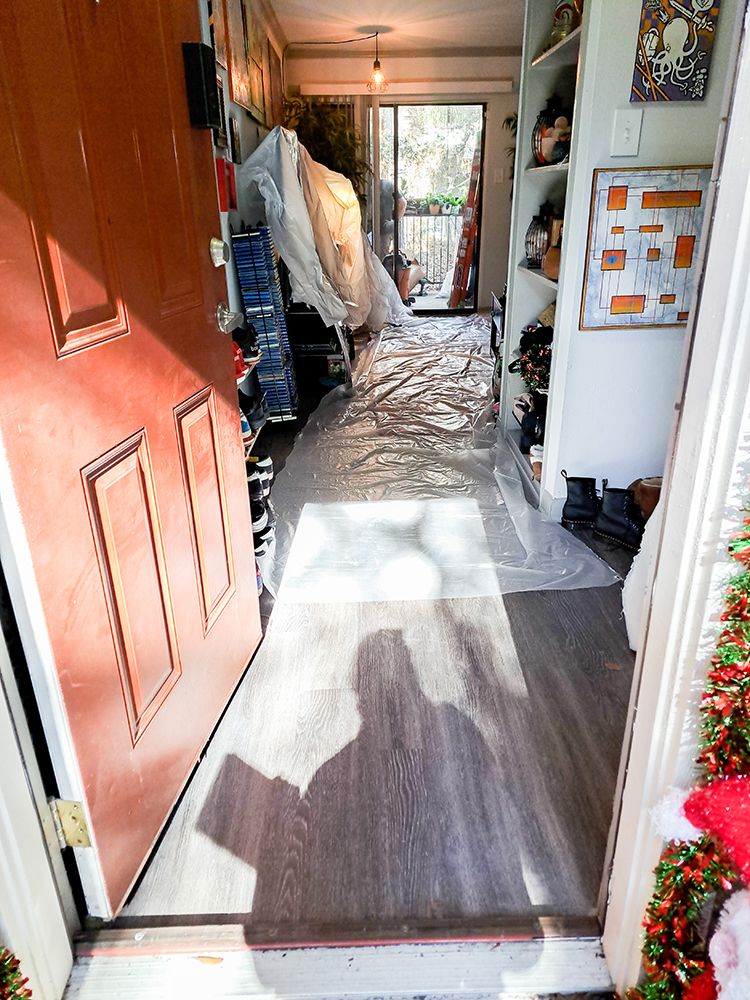 Apartment entryway with plastic sheeting covering the floor and furniture, indicating renovations or cleaning in progress.