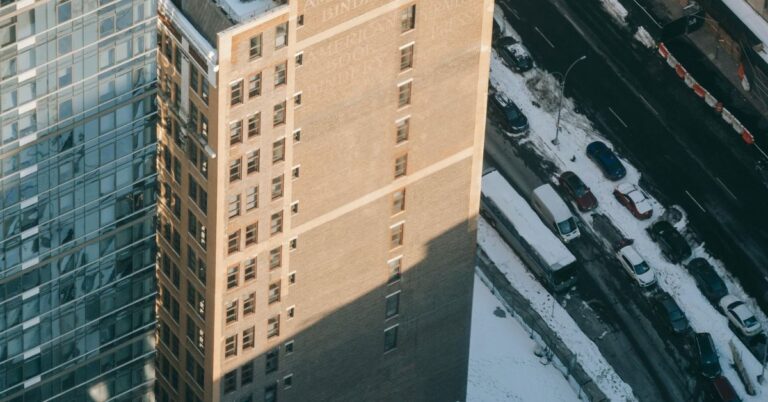 High-angle view of two buildings, one glass and one brick, with cars parked along a snow-covered street.
