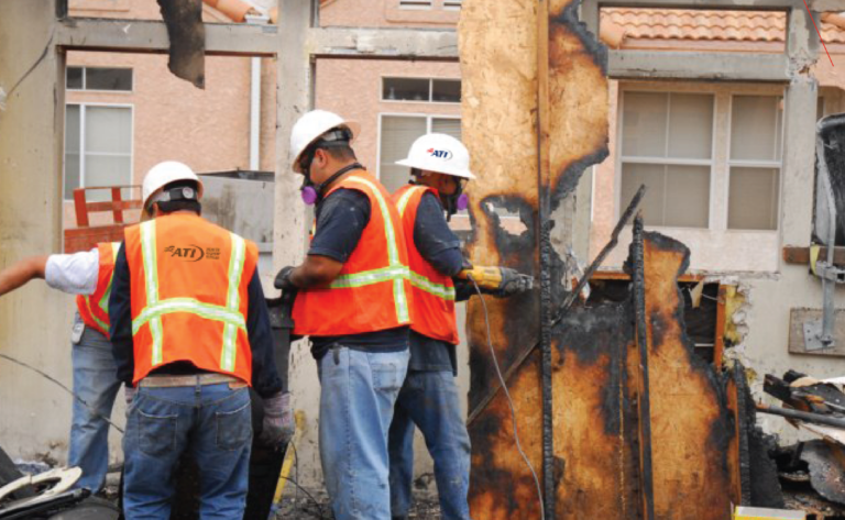 Three workers in safety gear are removing fire-damaged materials from a building.