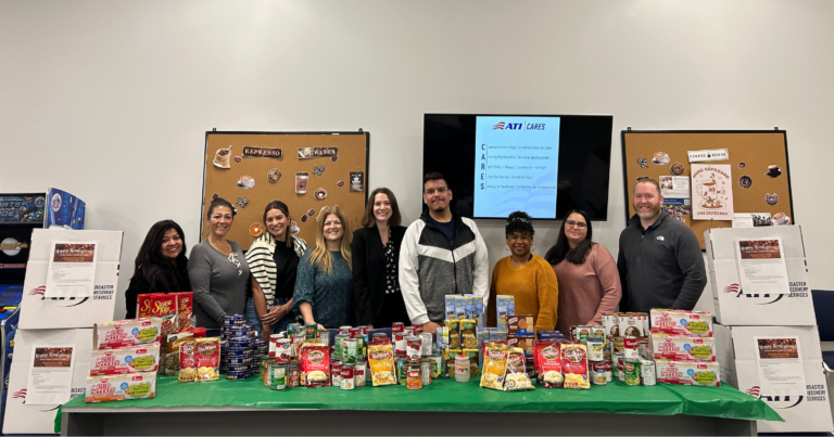 Group photo of ATI Cares employees posing with boxes and bags of food collected for a food drive.